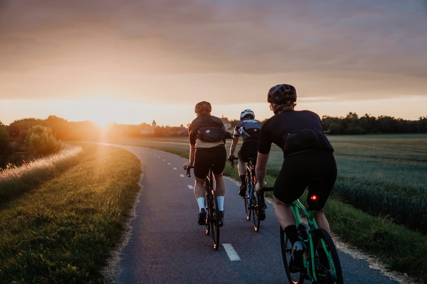 Radfahrer fahren bei Sonnenuntergang auf einem Feldweg.