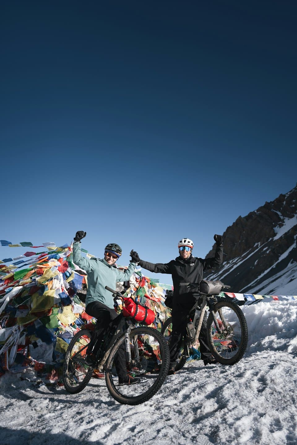Zwei Radfahrer feiern ihre Bergtour unter bunten Gebetsfahnen.