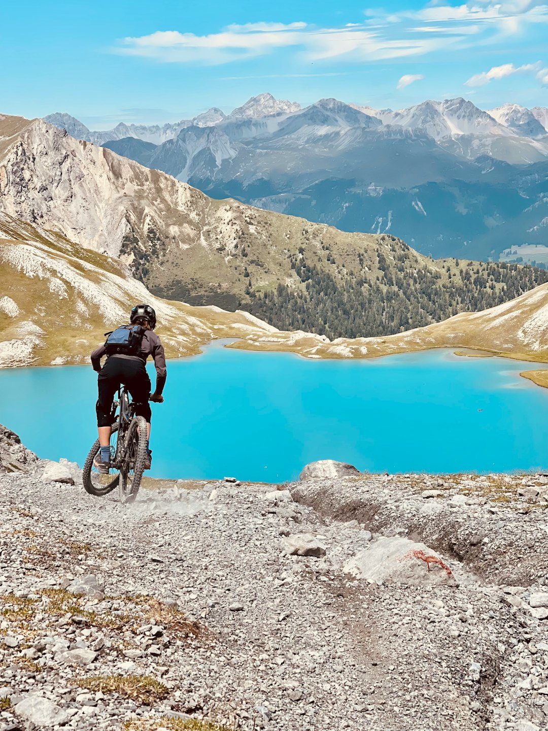 Mountainbiker fährt auf einem felsigen Trail über einem türkisfarbenen See.